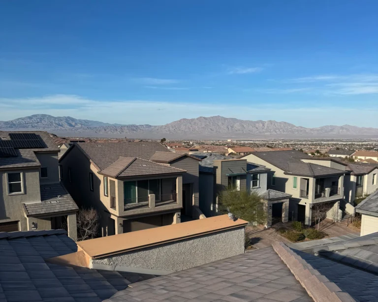 View over a hillside neighborhood of modern two-story tile-roof homes, some with rooftop solar panels, overlooking the valley and desert mountains under a clear blue sky in Nevada