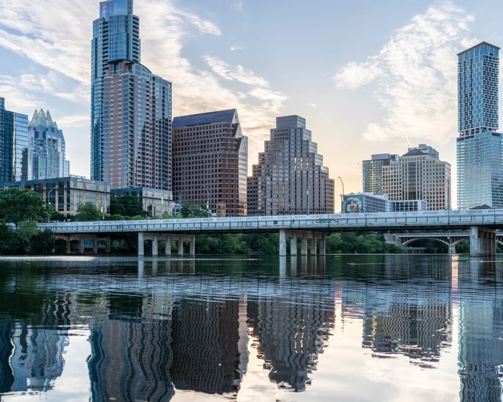 Downtown Austin high-rises, including the pointed Frost Bank Tower, reflected in Lady Bird Lake with a bridge crossing the water at dusk, Texas